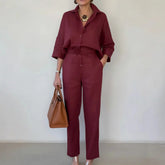 Woman in burgundy relaxed-fit linen shirt and high-waisted pants, holding a tan handbag