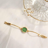 Gold bracelet watch with green dial and adjustable chain on white fabric background