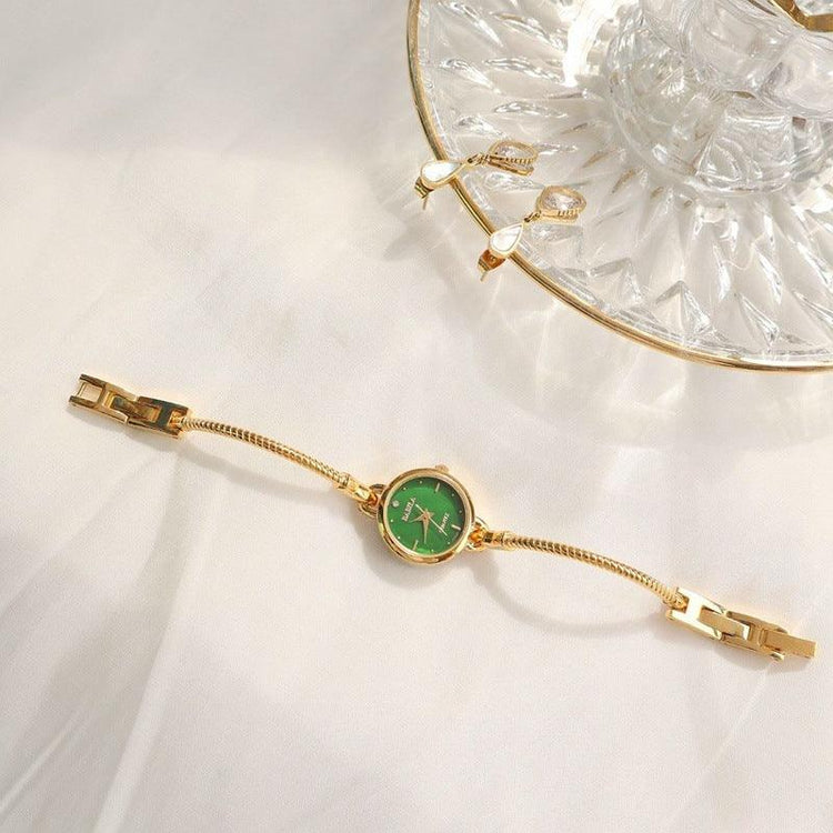Gold bracelet watch with green dial and adjustable chain on white fabric background