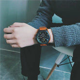 Person wearing gray knit sweater and black pants, orange leather strap wristwatch