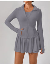 Woman wearing gray zip-up athletic jacket and pleated mini skirt, fitted activewear style