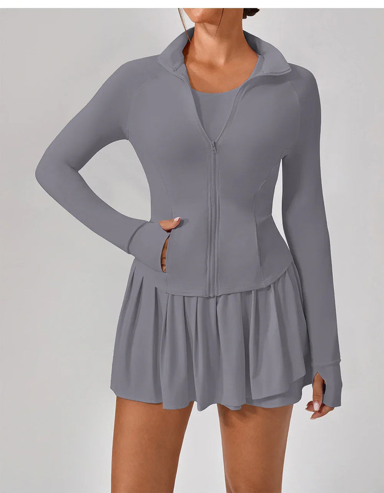 Woman wearing gray zip-up athletic jacket and pleated mini skirt, fitted activewear style