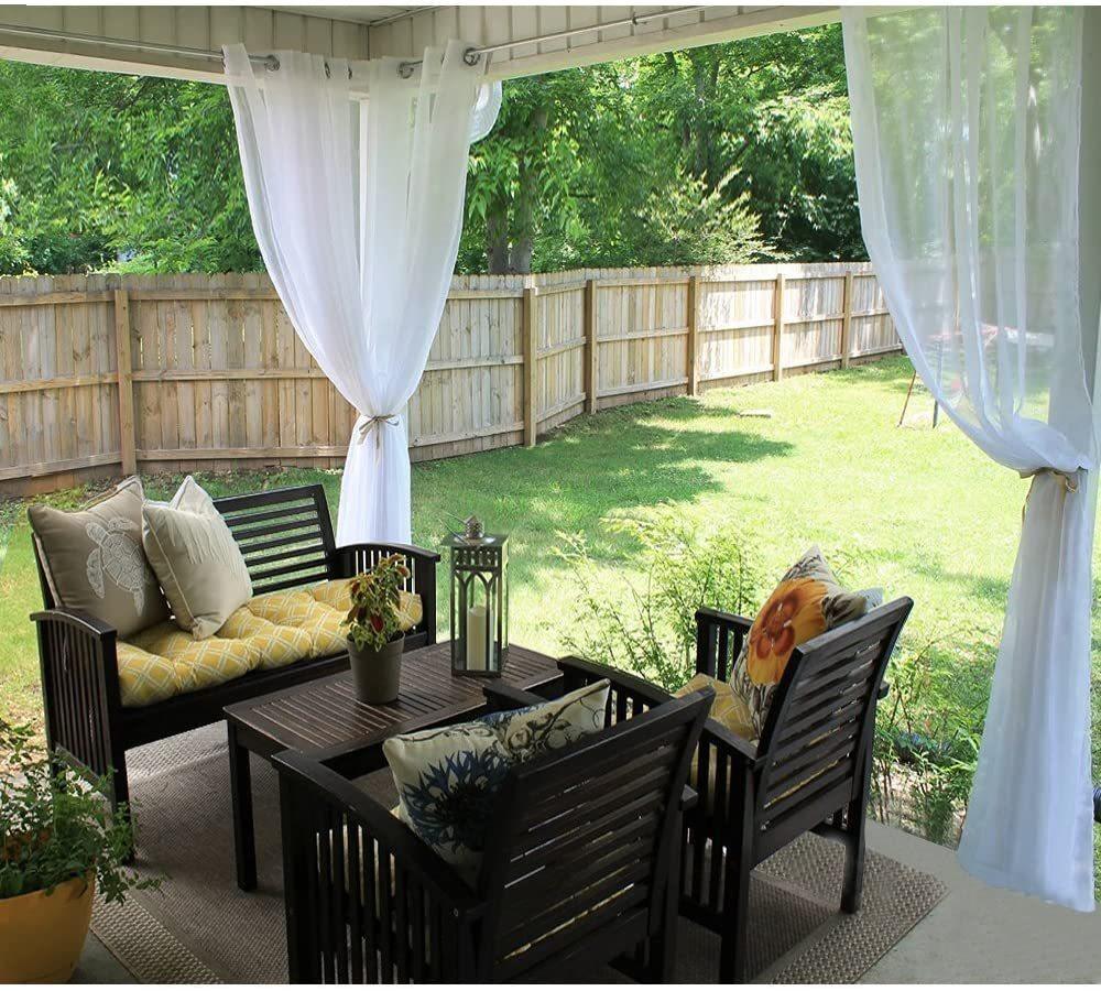 Outdoor patio set with dark wood chairs, yellow and beige cushions, white sheer curtains, and decorative pillows.