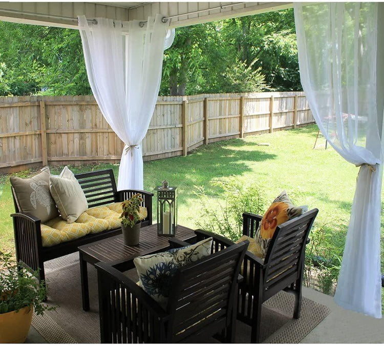 Outdoor patio set with dark wood chairs, yellow and beige cushions, white sheer curtains, and decorative pillows.
