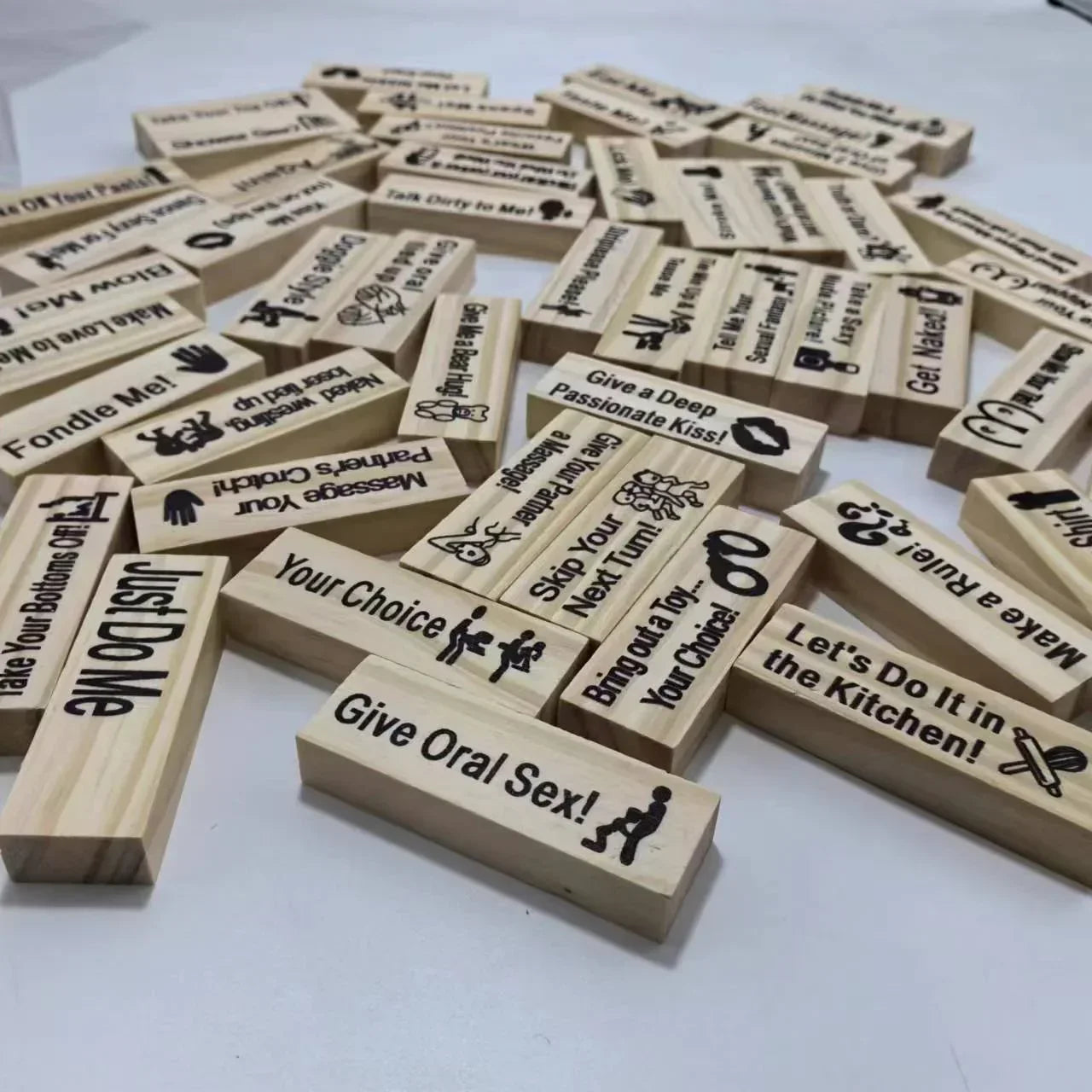 Scattered wooden game blocks with adult-themed phrases engraved, displayed on a white surface.
