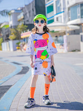 Child wearing oversized streetwear t-shirt dress with colorful graphic print, neon socks, chunky sneakers, and neon cap