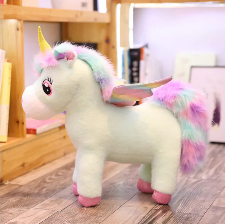 Plush pastel unicorn toy with rainbow mane, wings, and pink hooves on wood floor