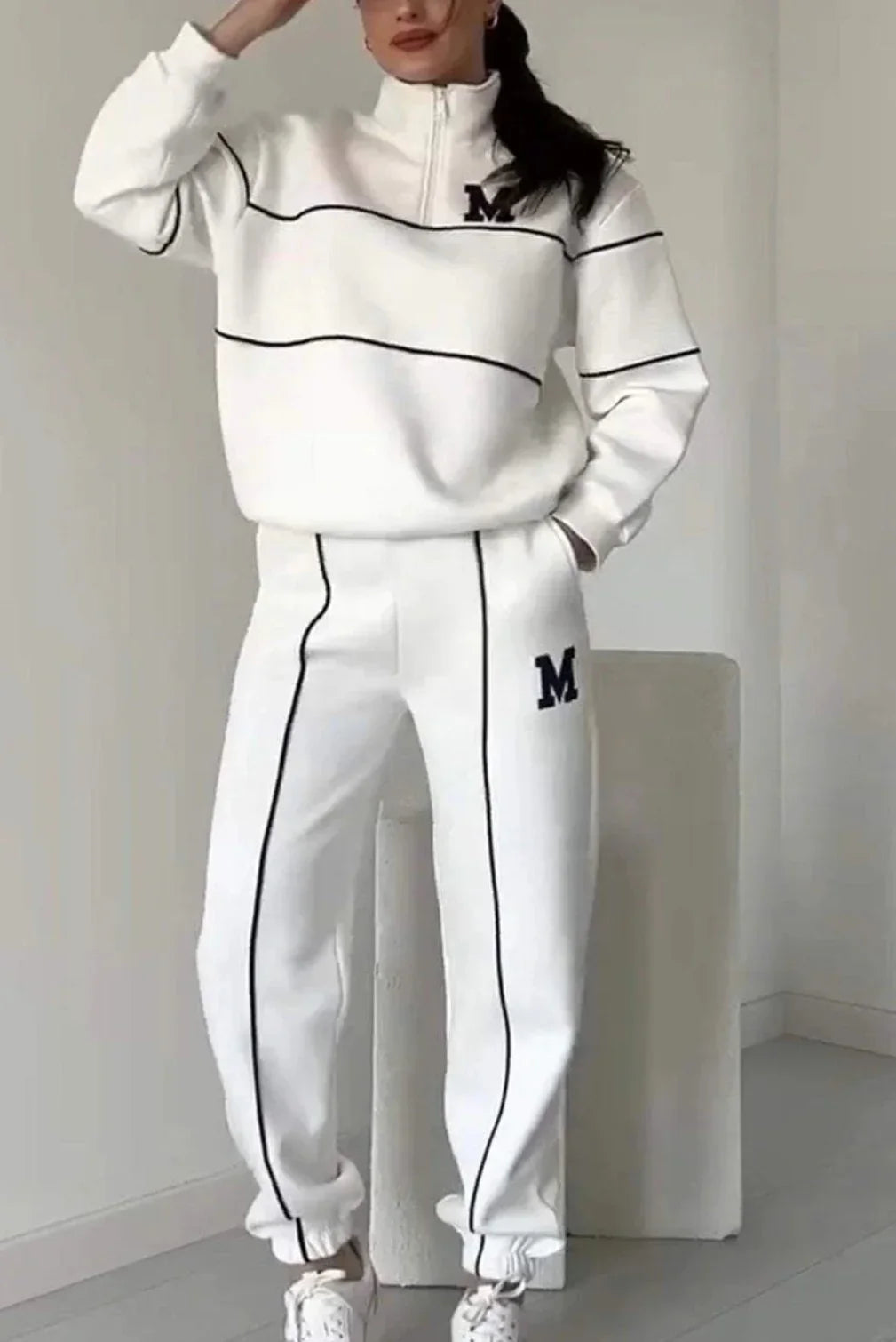Woman wearing a white relaxed-fit tracksuit with black piping and M logo, sporty streetwear