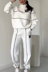 Woman wearing a white relaxed-fit tracksuit with black piping and M logo, sporty streetwear