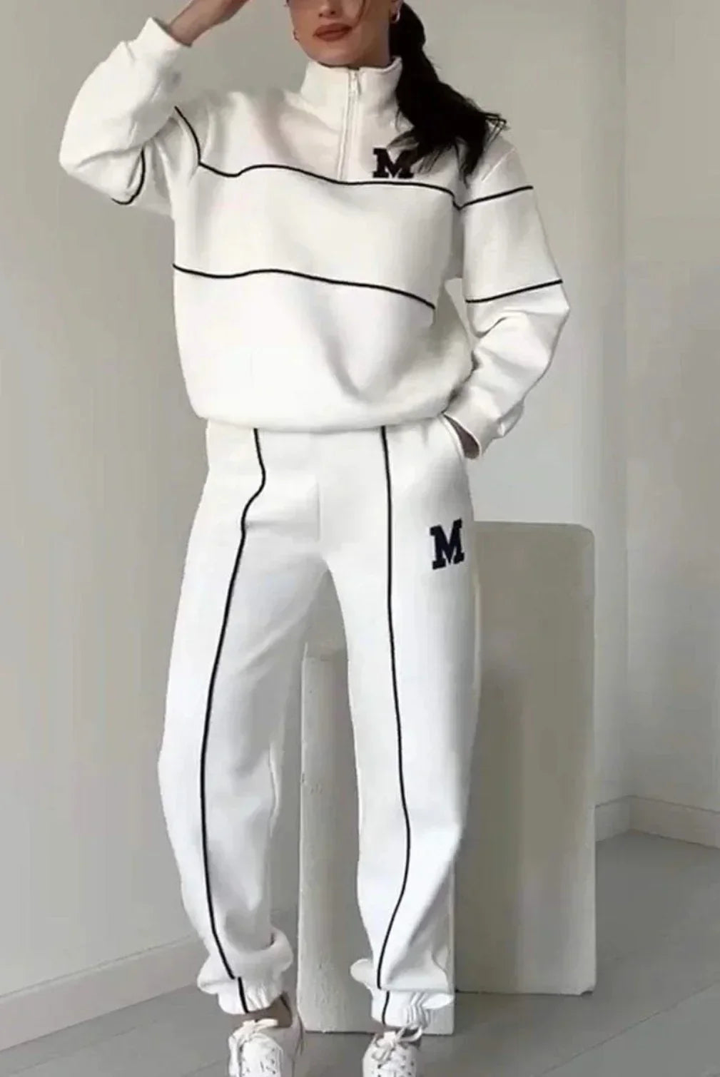 Woman wearing a white relaxed-fit tracksuit with black piping and M logo, sporty streetwear