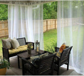 Outdoor patio with sheer white curtains, dark wood furniture, and colorful cushions