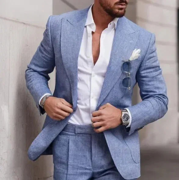 Man wearing slim-fit light blue linen suit with white shirt, pocket square, and sunglasses.