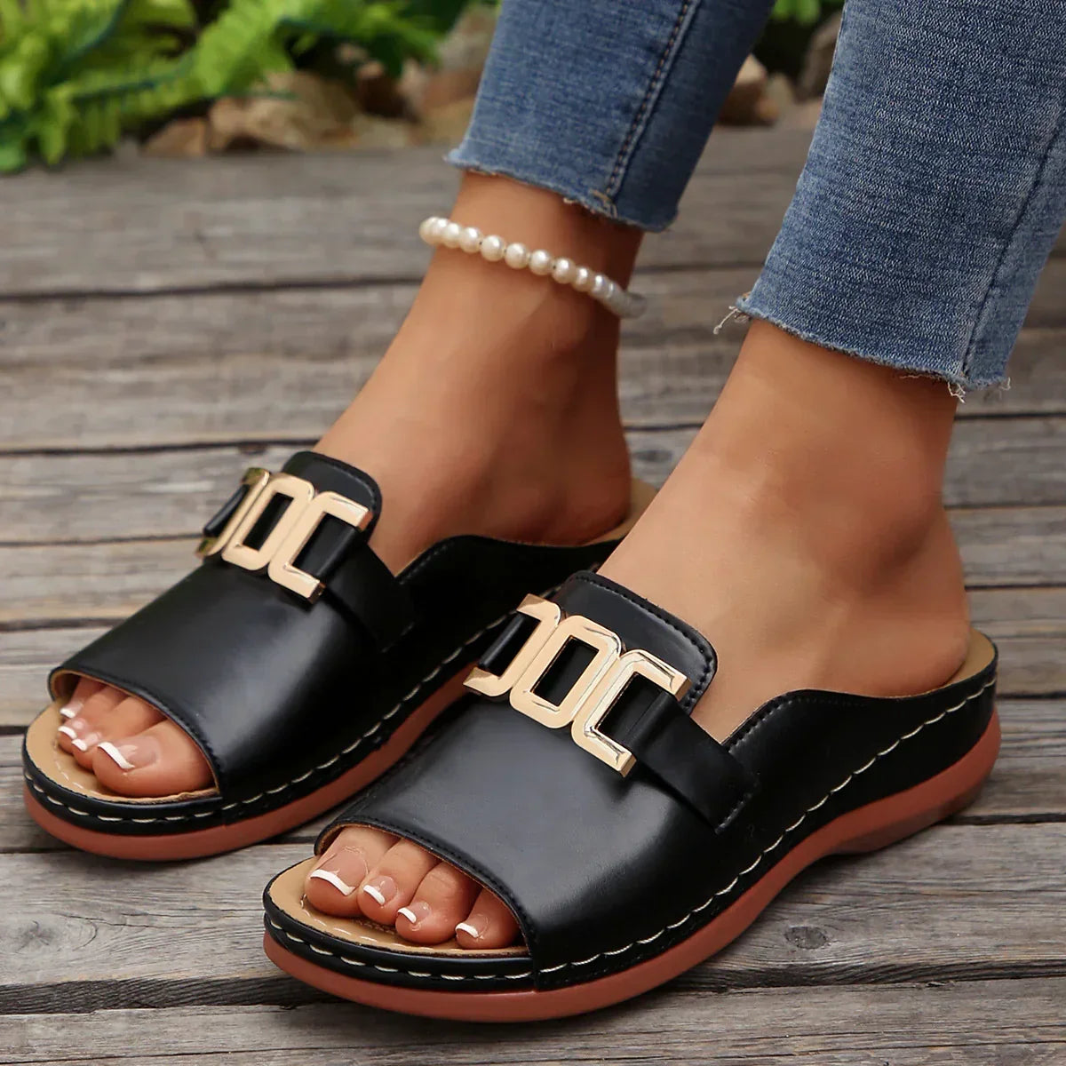 Black open-toe slide sandals with gold buckle detail and cushioned sole, styled with jeans