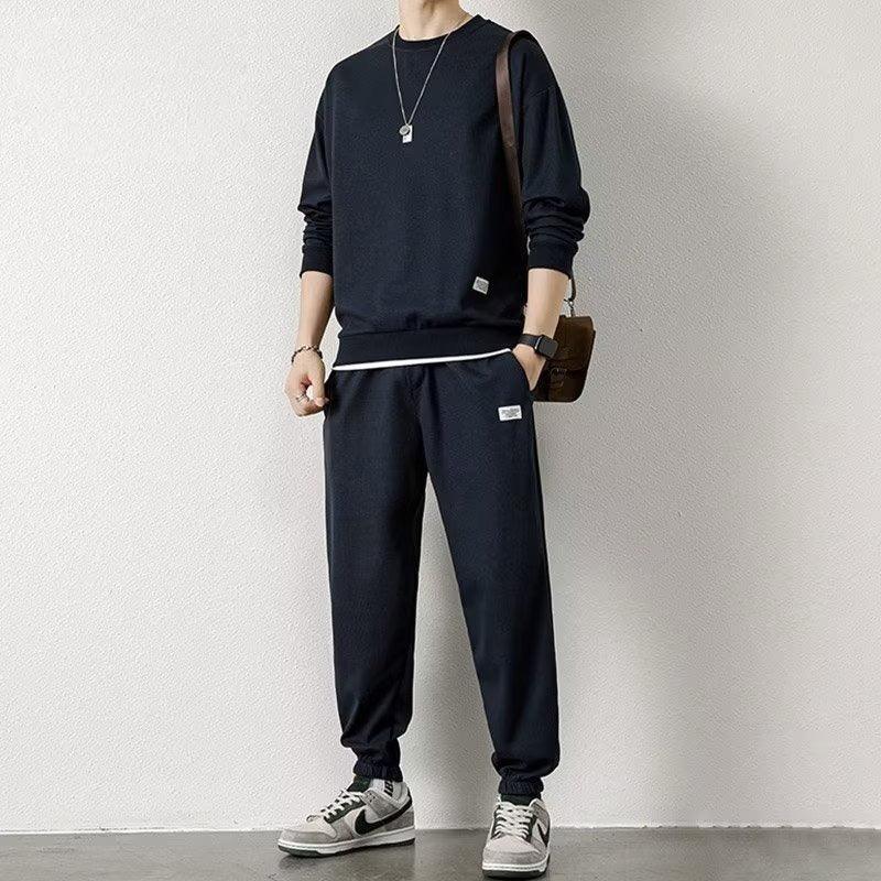Man wearing black streetwear jogger set with relaxed fit and white sneakers in minimal setting