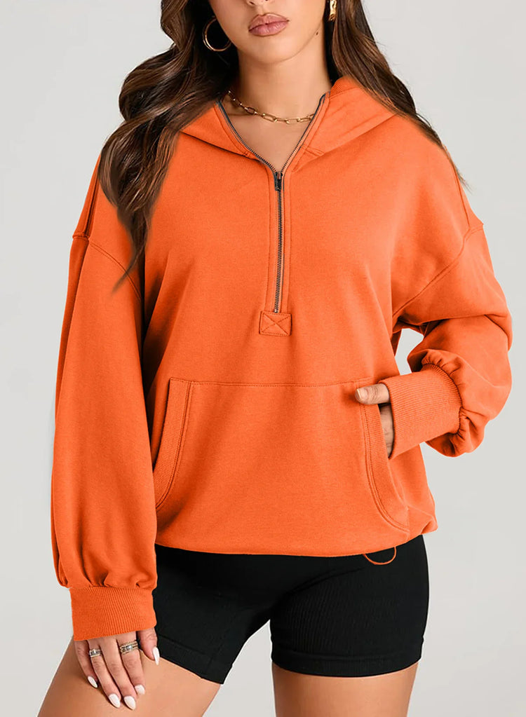 Woman wearing an oversized orange zip hoodie with kangaroo pocket and black biker shorts