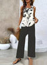 Woman wearing a sleeveless white and black print top with wide-leg black pants and sandals.
