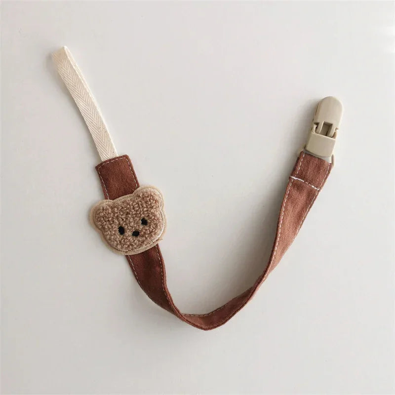 Brown fabric pacifier clip with plush teddy bear accent and plastic clasp