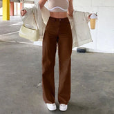 Woman in high-waisted brown wide-leg pants, white crop top, cream jacket, and white sneakers