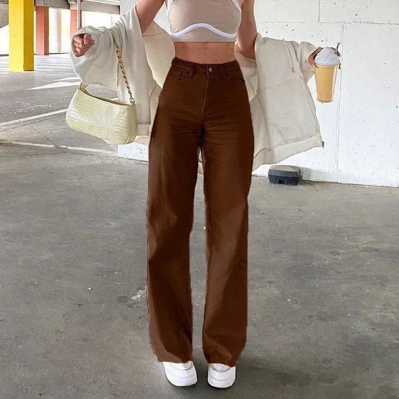 Woman in high-waisted brown wide-leg pants, white crop top, cream jacket, and white sneakers