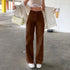 Woman in high-waisted brown wide-leg pants, white crop top, cream jacket, and white sneakers