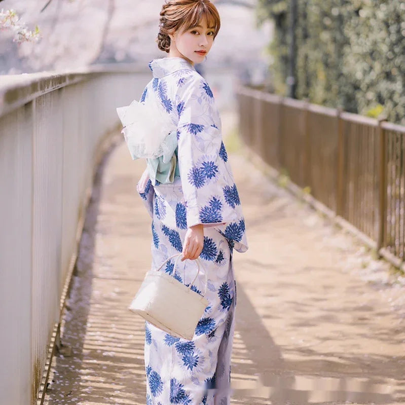 Woman wearing a blue and white floral kimono, holding a small handbag, standing outdoors