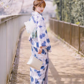 Woman wearing a blue and white floral kimono, holding a small handbag, standing outdoors
