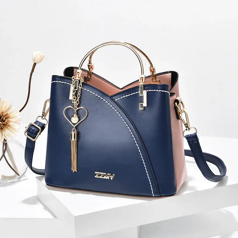 Elegant blue and pink faux leather handbag with gold hardware, top handle, and crossbody strap