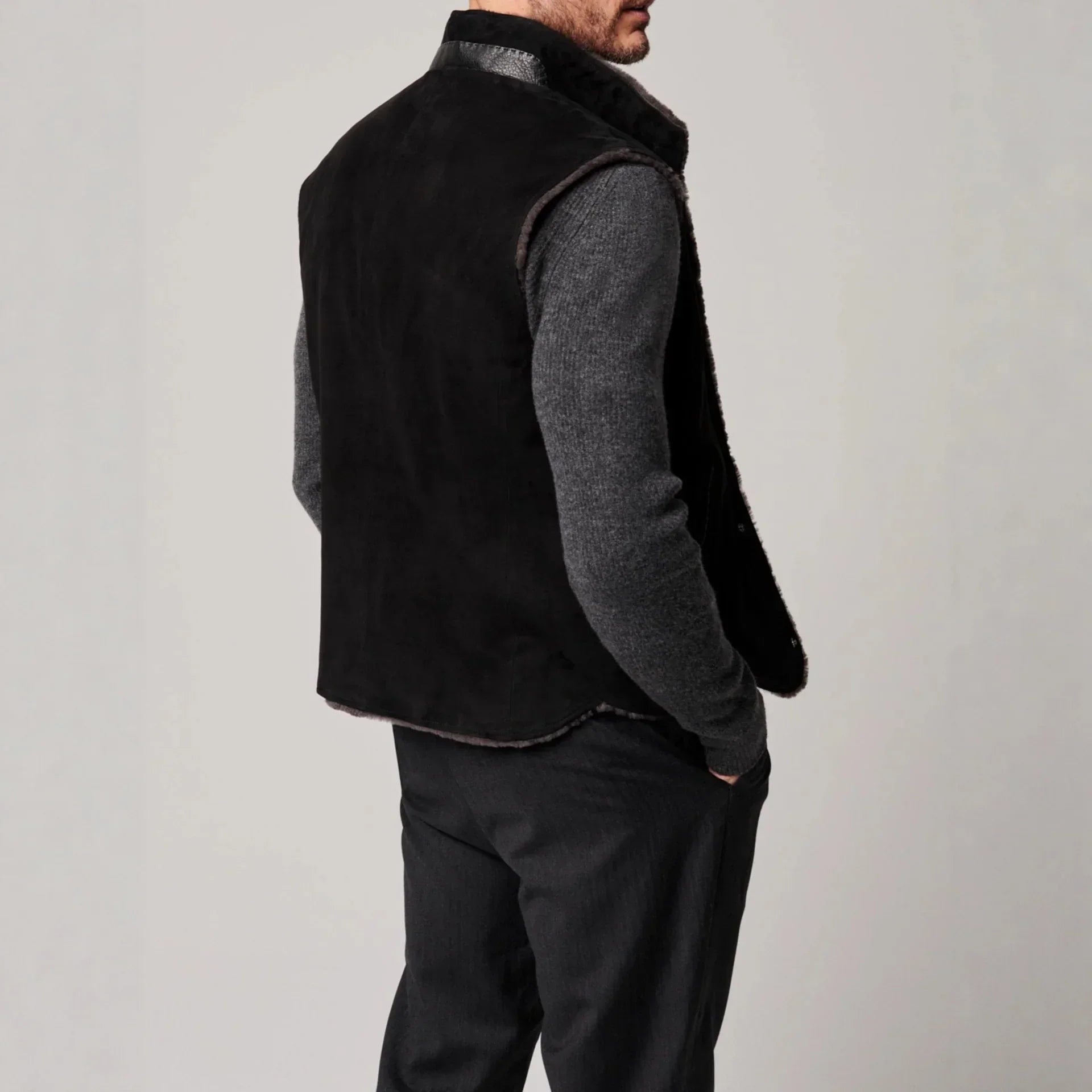 Man wearing a black shearling vest over a gray knit sweater with relaxed fit, side view