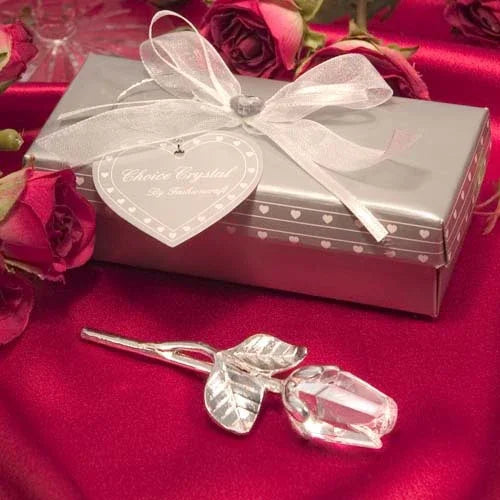 Crystal rose ornament displayed on red satin fabric beside a silver gift box and red roses