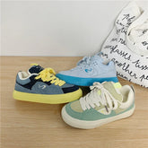 Three pairs of low-top suede sneakers in pastel blue, green, and yellow color block styles on wood surface.