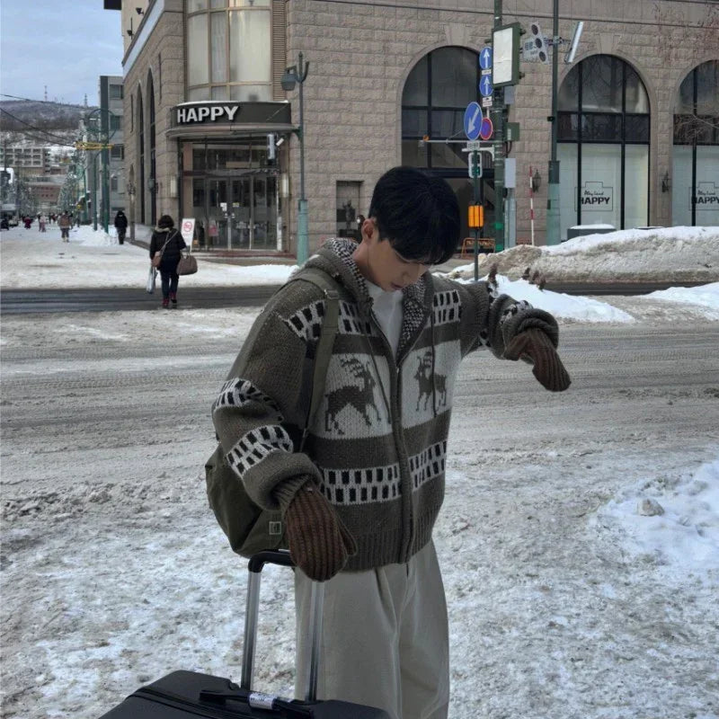 Man in oversized knit zip-up sweater with deer pattern, brown mittens, and wide-leg pants in snowy urban street