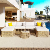 Modern outdoor patio set with beige rattan frame, white cushions, yellow pillows, and round table
