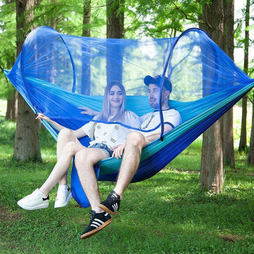 Couple wearing casual streetwear, shorts, and sneakers relaxing in a blue hammock with netting outdoors
