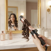 Woman using rose gold ceramic curling iron for loose curls in modern bathroom