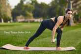 Woman in black athletic leggings and sports bra stretching on a yoga mat outdoors