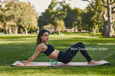 Woman in black fitted workout leggings and sports bra using a mini foam roller outdoors on a yoga mat
