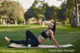 Woman in black sports bra and leggings on yoga mat outdoors, fitted activewear, stretching.